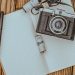 Flat lay of a retro camera on a wooden table with a notepad and film roll.