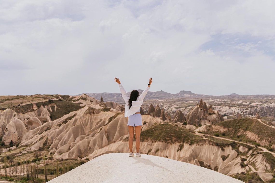 A woman raises her arms in celebration amidst the stunning landscapes of Cappadocia.
