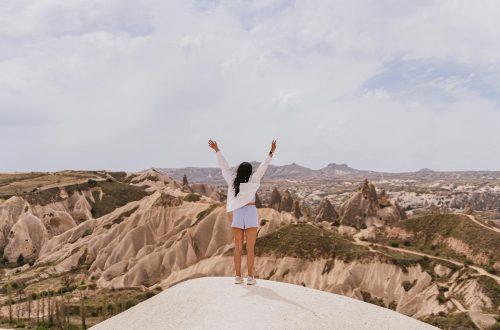 A woman raises her arms in celebration amidst the stunning landscapes of Cappadocia.